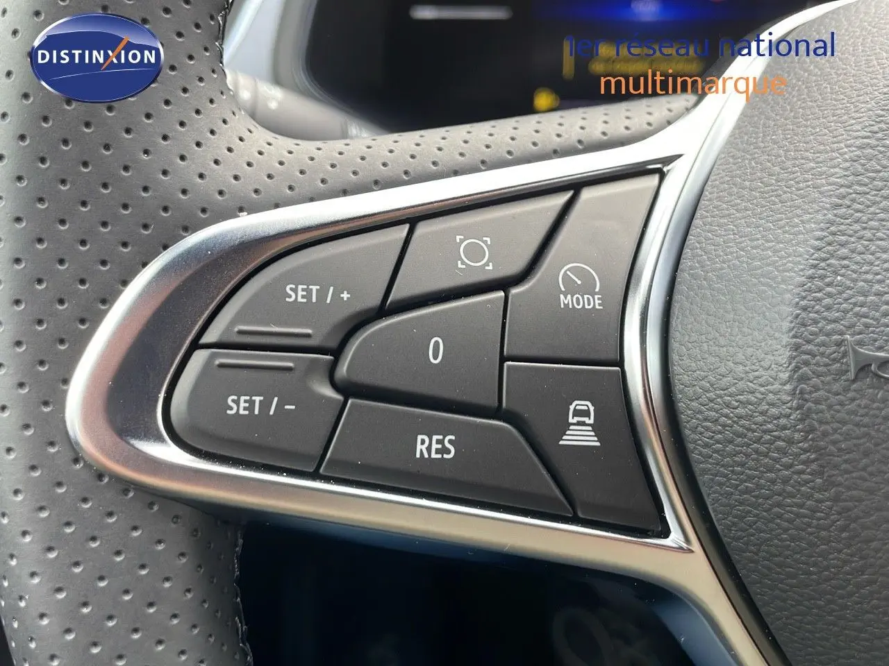 Gros plan sur les commandes de régulateur de vitesse au volant perforé du Renault Captur E-Tech hybride rouge toit noir.