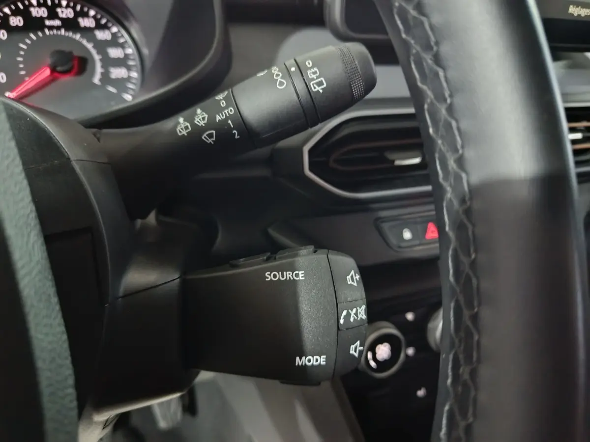 Gros plan sur la commande multifonctions du volant cuir synthétique de la Dacia Sandero Extreme+ bleu, tableau de bord en arrière-plan.