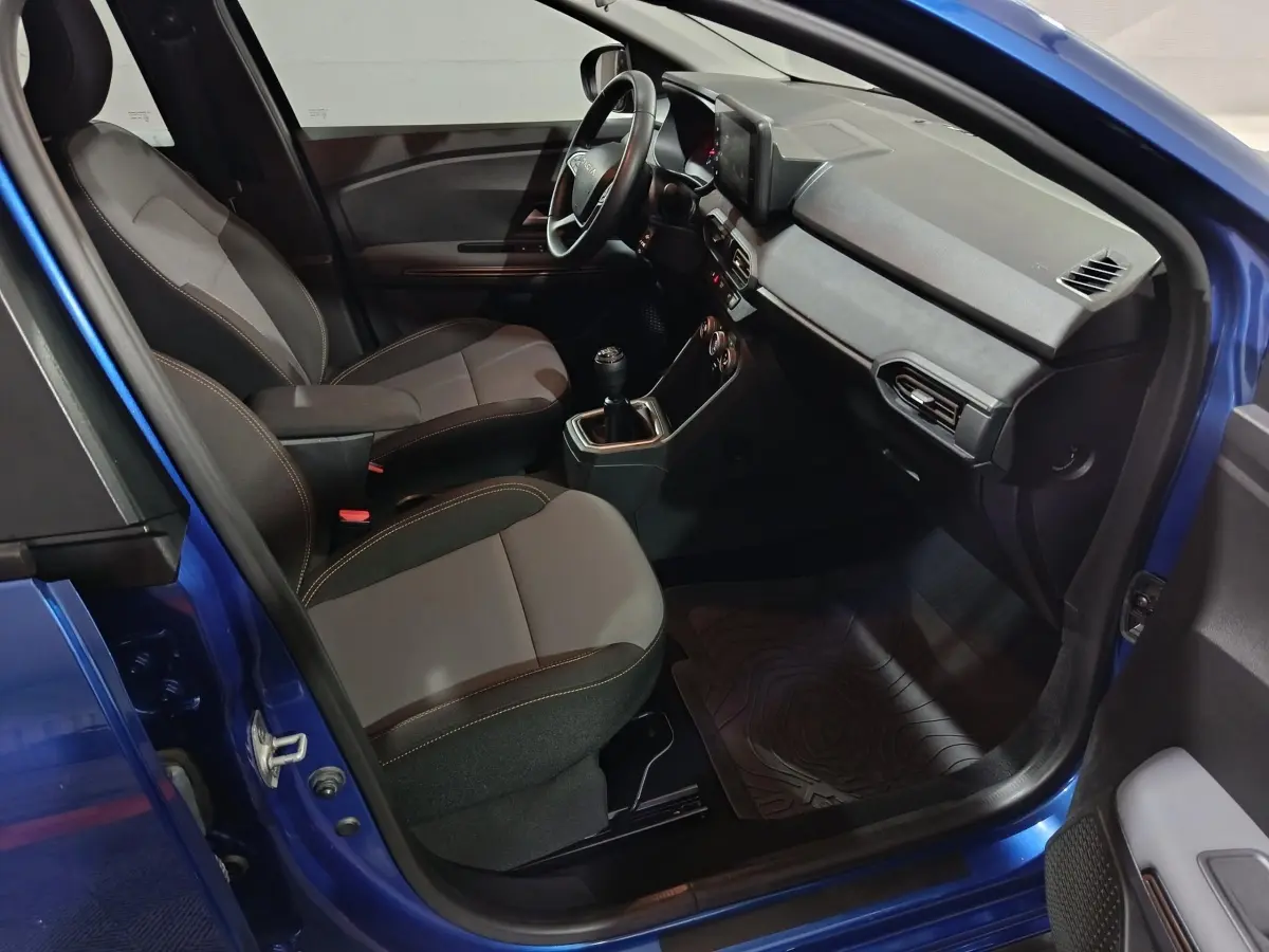 Vue intérieure côté conducteur de la Dacia Sandero Extreme+ bleu 2024, avec sièges tissu bicolore et volant multifonctions cuir synthétique.