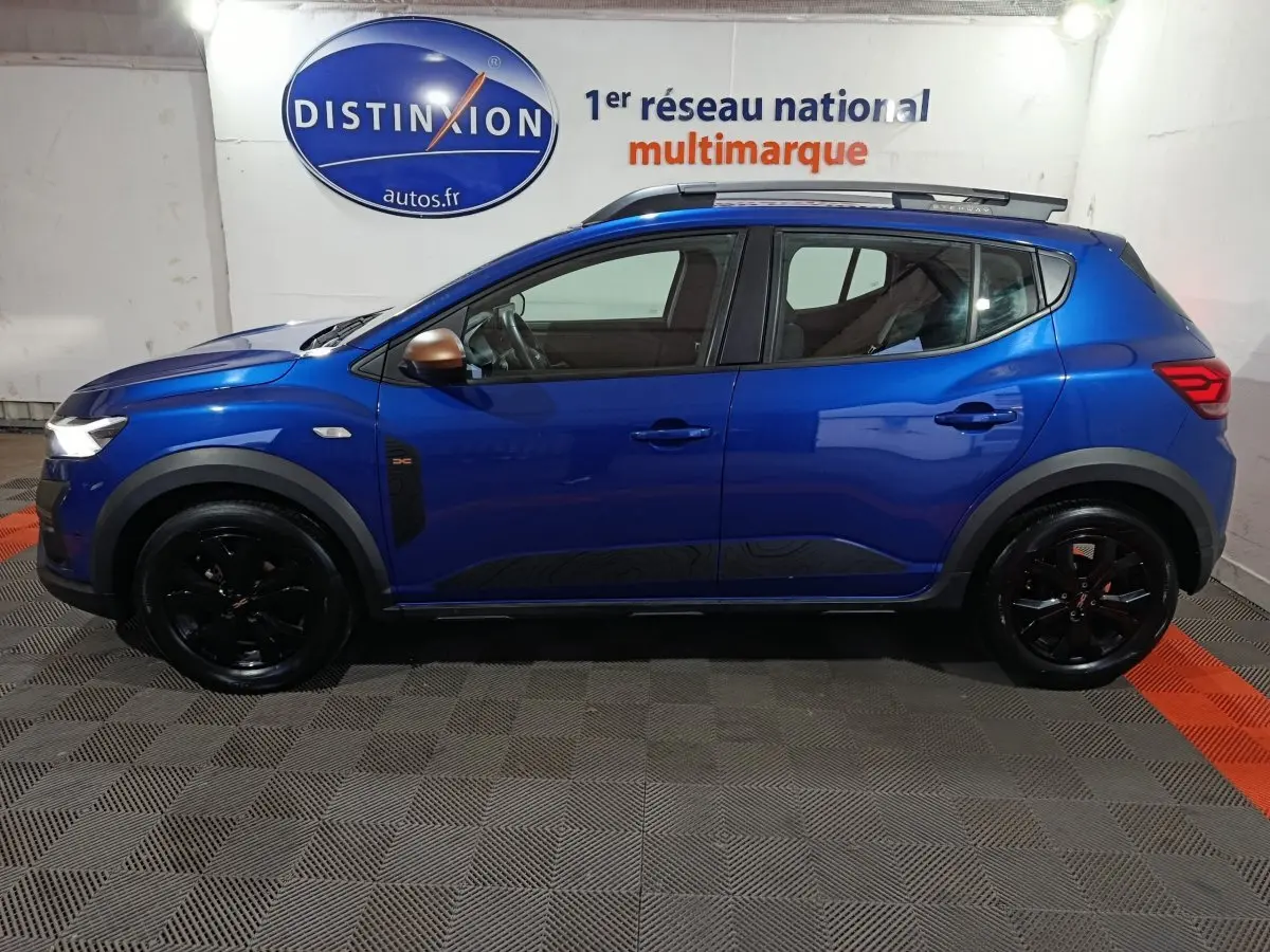Vue de profil côté gauche d'une Dacia Sandero Extreme+ TCe 110 bleu avec jantes noires et rétroviseurs cuivrés.