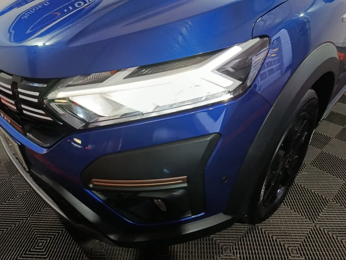 Gros plan sur l'avant droit bleu d'une Dacia Sandero Extreme+ 2024, avec phare LED et détails noirs et cuivrés.