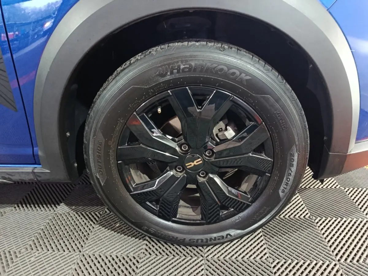Gros plan sur la roue avant gauche noire brillante d’une Dacia Sandero Extreme+ bleu 2024 avec jante design.