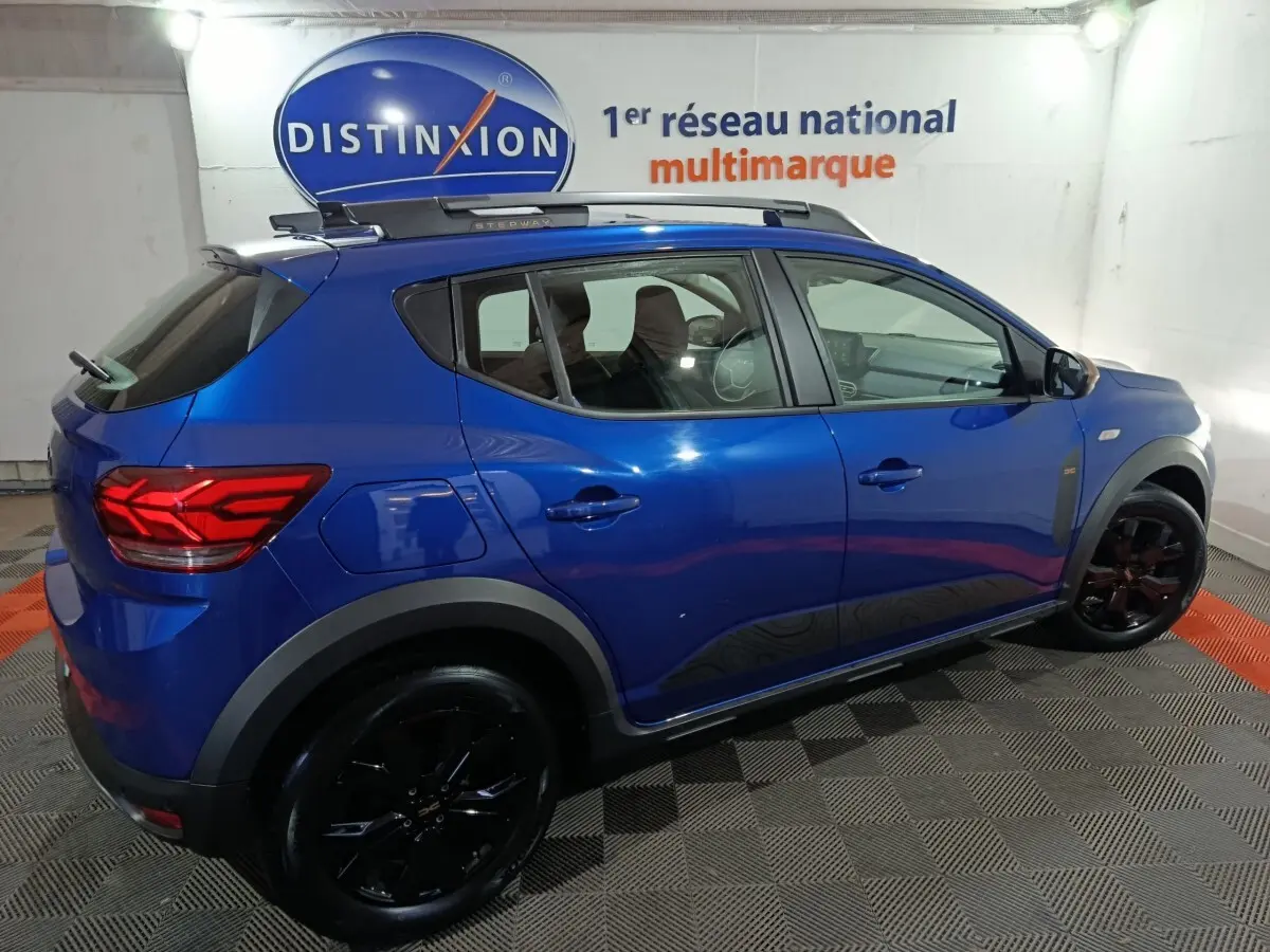 Vue latérale droite d'une Dacia Sandero Extreme+ TCe 110 2024 bleu avec jantes noires et barres de toit assorties.