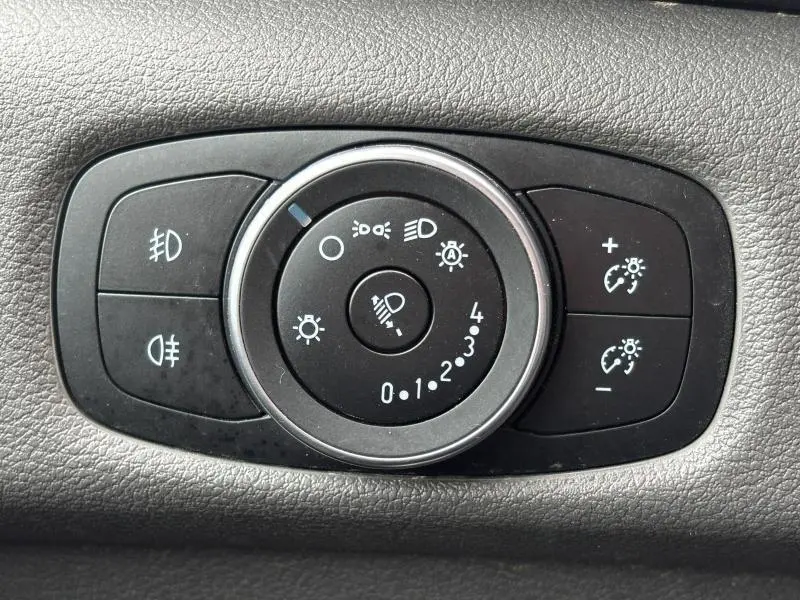 Gros plan sur le bouton de réglage des phares du Ford Transit Fourgon blanc glacier, avec commandes d'éclairage et de réglage d'intensité.