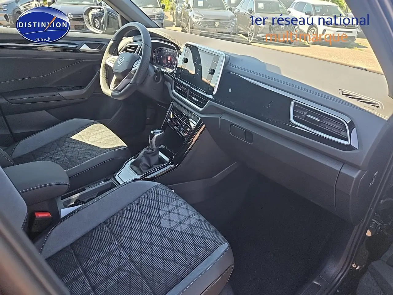 Intérieur du Volkswagen T-Roc 2025 vu côté passager, sièges tissu noir à motifs, tableau de bord moderne et écran tactile.