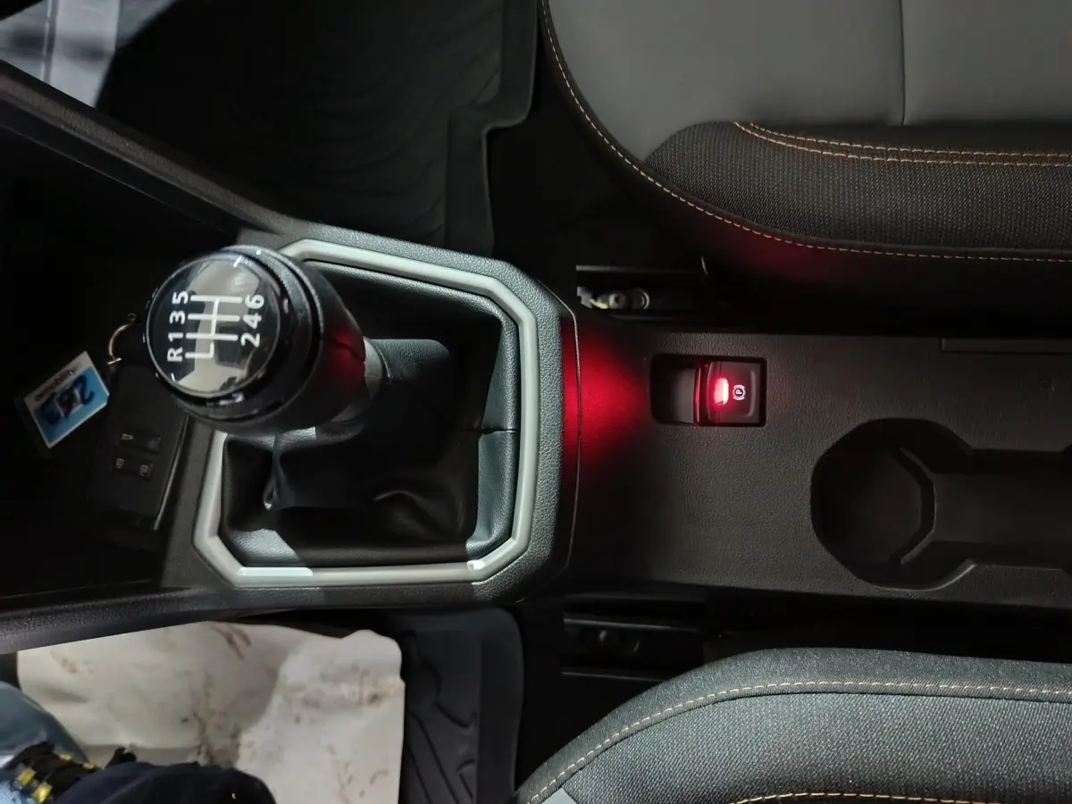 Vue rapprochée de la console centrale noire avec levier de vitesse manuel et frein à main électrique rouge d’une Dacia Sandero bleu 2024.