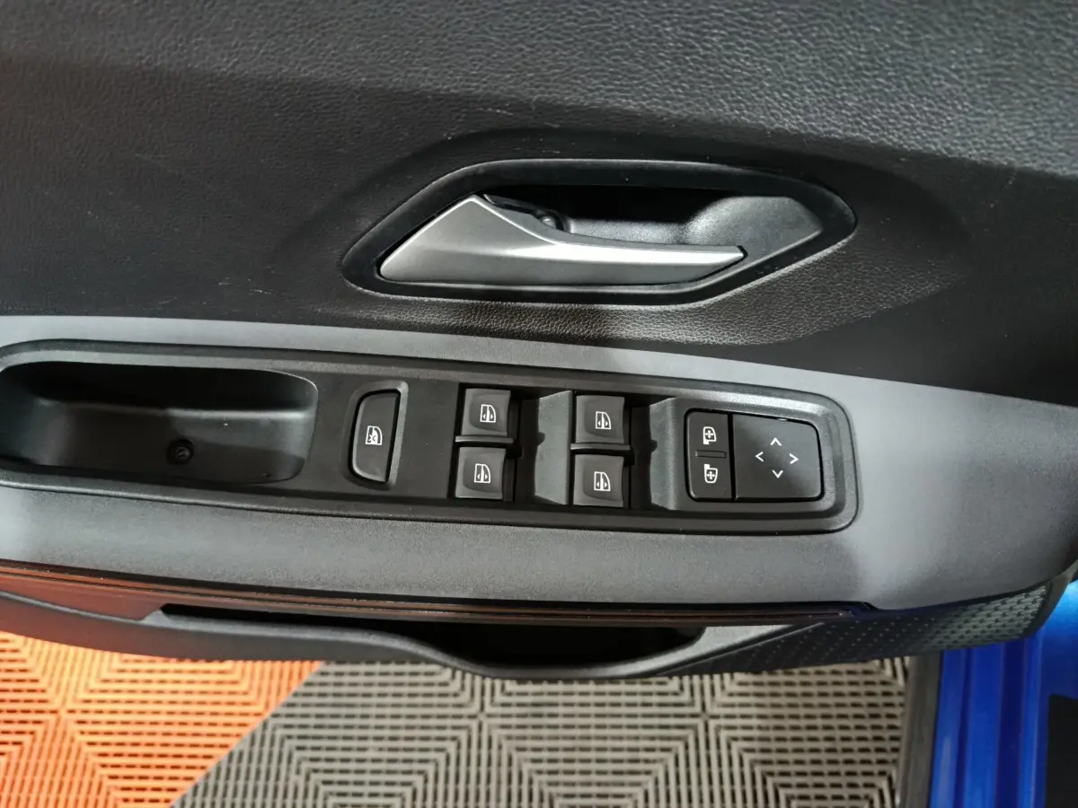 Gros plan sur la commande des vitres et la poignée intérieure côté gauche d'une Dacia Sandero bleu 2024.