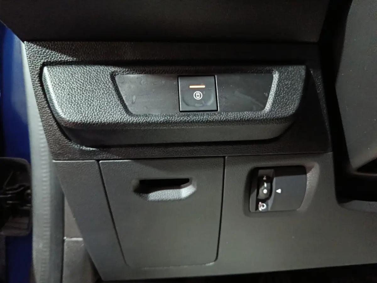 Détail intérieur montrant le bouton de verrouillage central et commandes sur la console inférieure d’une Dacia Sandero bleu.