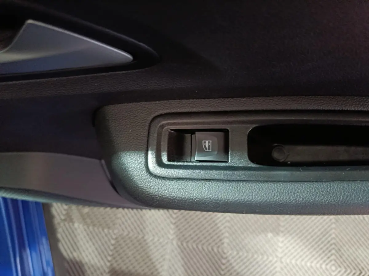 Gros plan sur le bouton de commande de la vitre électrique côté conducteur d'une Dacia Sandero bleu 2024.