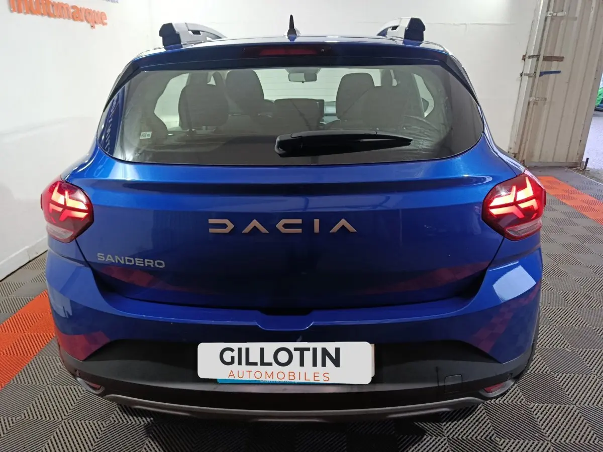 Vue arrière d'une Dacia Sandero Extreme+ TCe 110 2024 en bleu avec feux arrière allumés et logo visible.