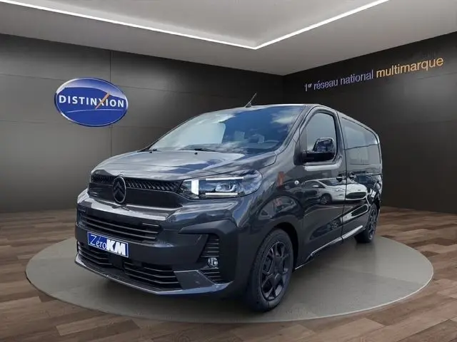 Vue 3/4 avant d'un Citroën Jumpy gris foncé, avec calandre noire et jantes sombres, en intérieur showroom.