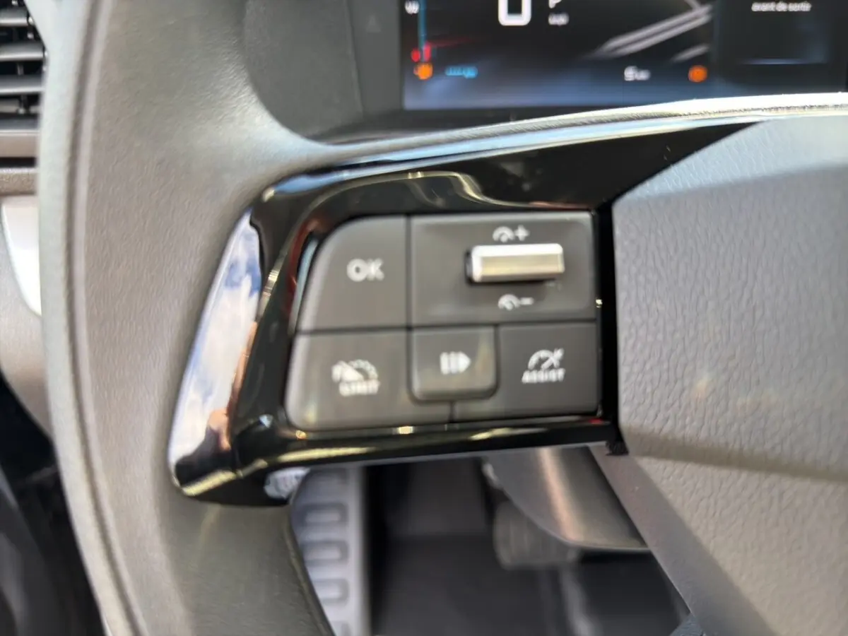 Gros plan sur les commandes multifonctions noires du volant côté gauche dans l'habitacle d'un Citroën Jumpy gris foncé.