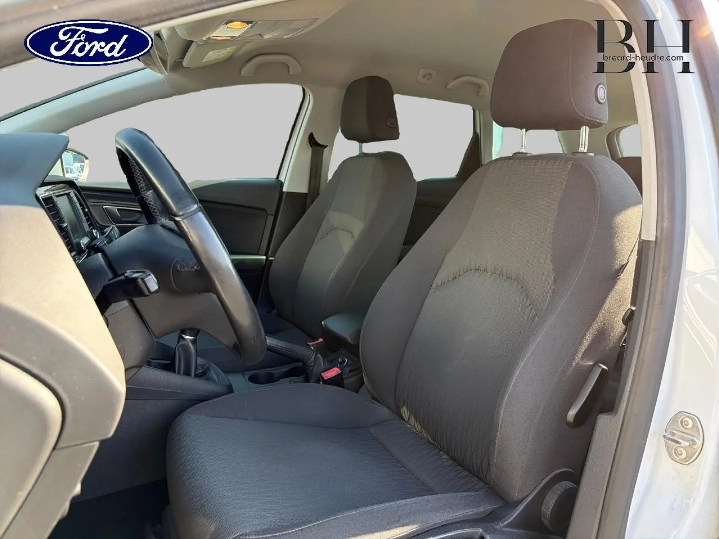 Vue intérieure côté conducteur d'une SEAT LEON ST gris étoile, montrant les sièges avant en tissu noir et le volant multifonction.
