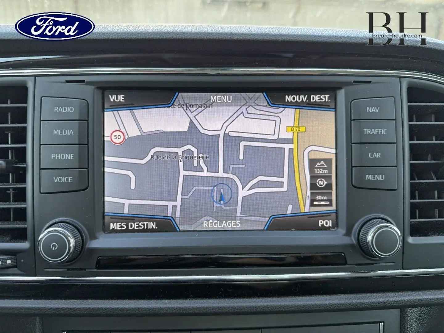 Écran tactile de navigation GPS sur tableau de bord d’une Ford, avec boutons de commande autour et logo Ford visible.