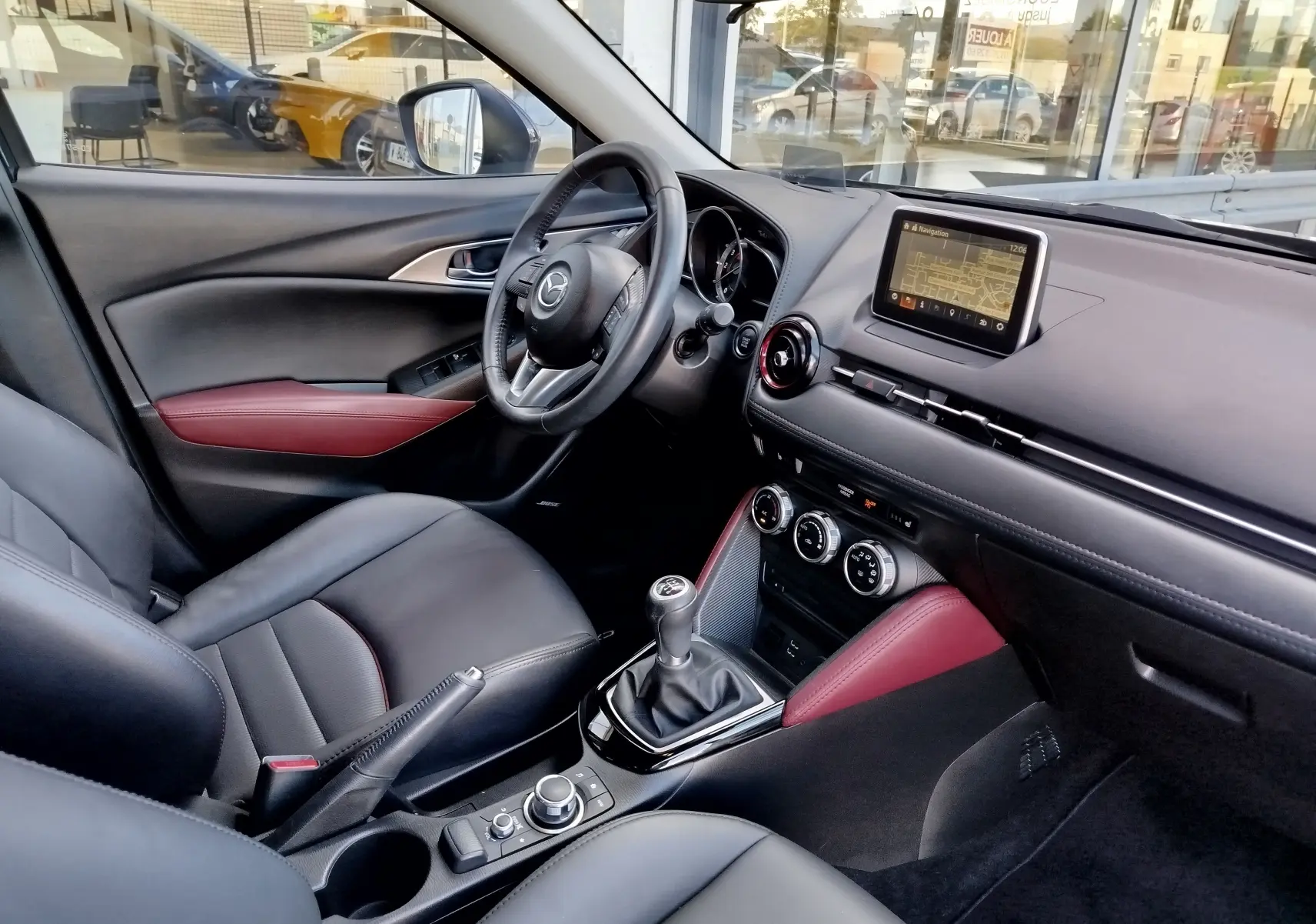 Intérieur du Mazda CX-3 2016 en vue côté conducteur, cuir noir avec surpiqûres rouges et écran tactile central.