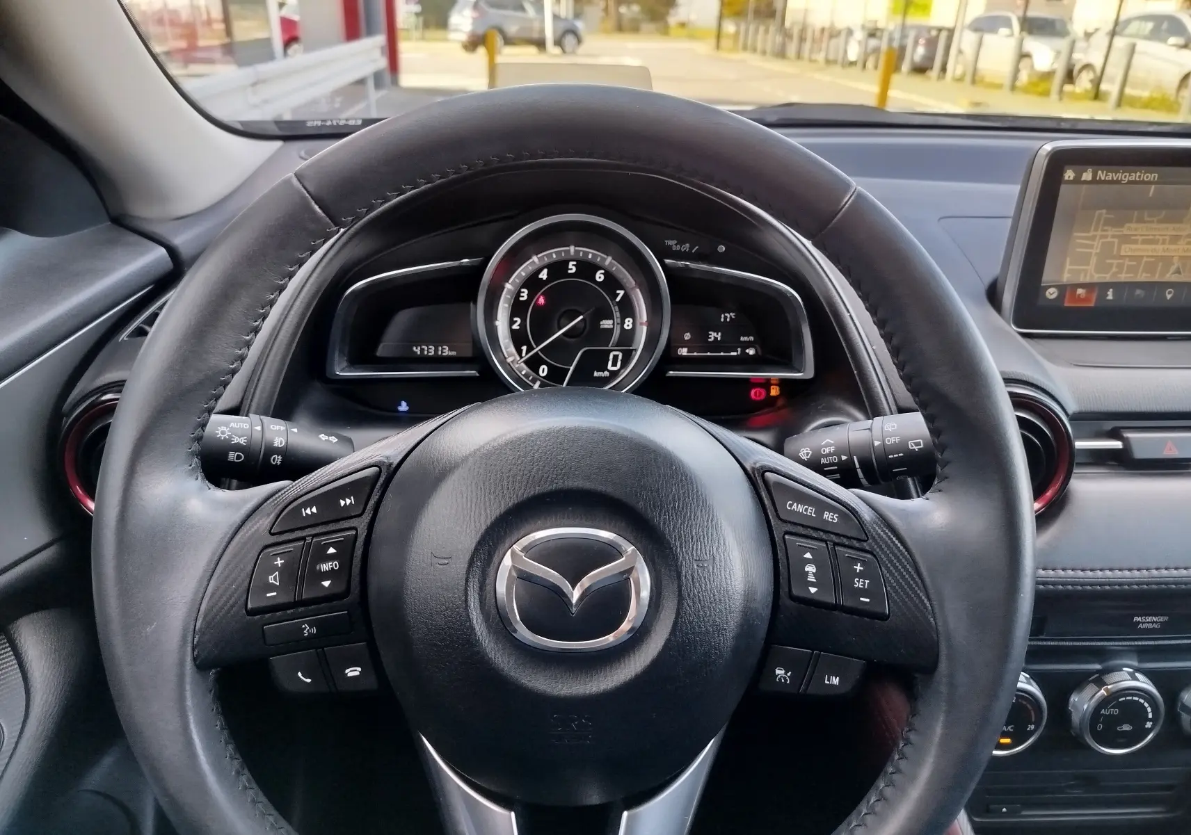 Vue rapprochée du volant en cuir noir et du tableau de bord du Mazda CX-3 2016 avec écran de navigation allumé.