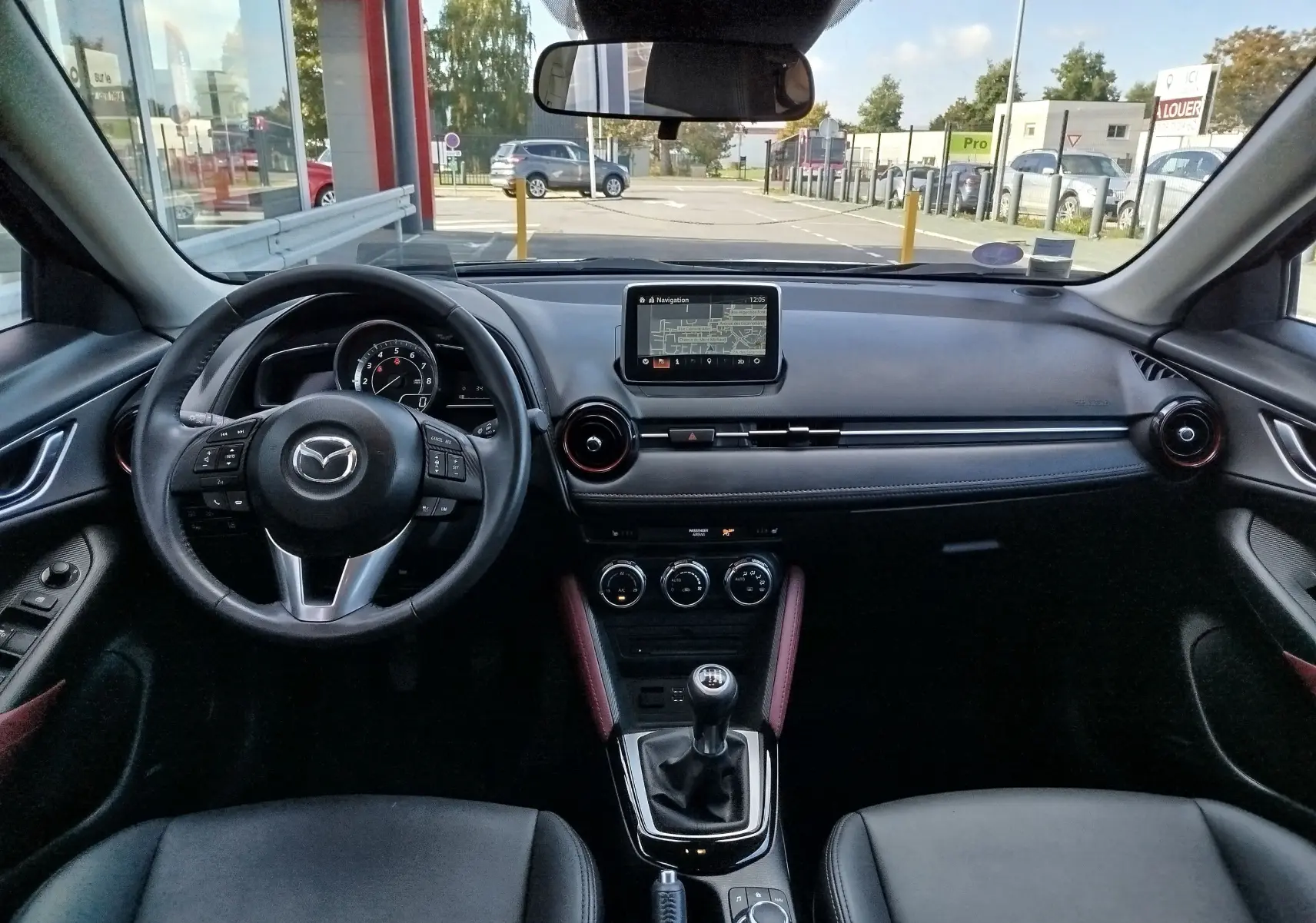 Vue intérieure avant du Mazda CX-3 2016, tableau de bord noir avec écran central et volant multifonction.