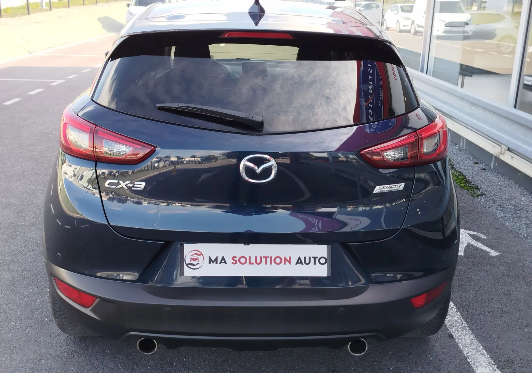 Vue arrière d'un Mazda CX-3 bleu Dynamic Blue Mica avec feux LED et double sortie d'échappement visible.