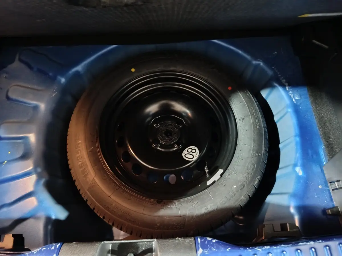 Roue de secours galette noire dans le coffre bleu d'une Dacia Sandero Extreme+ TCe 110 2024.
