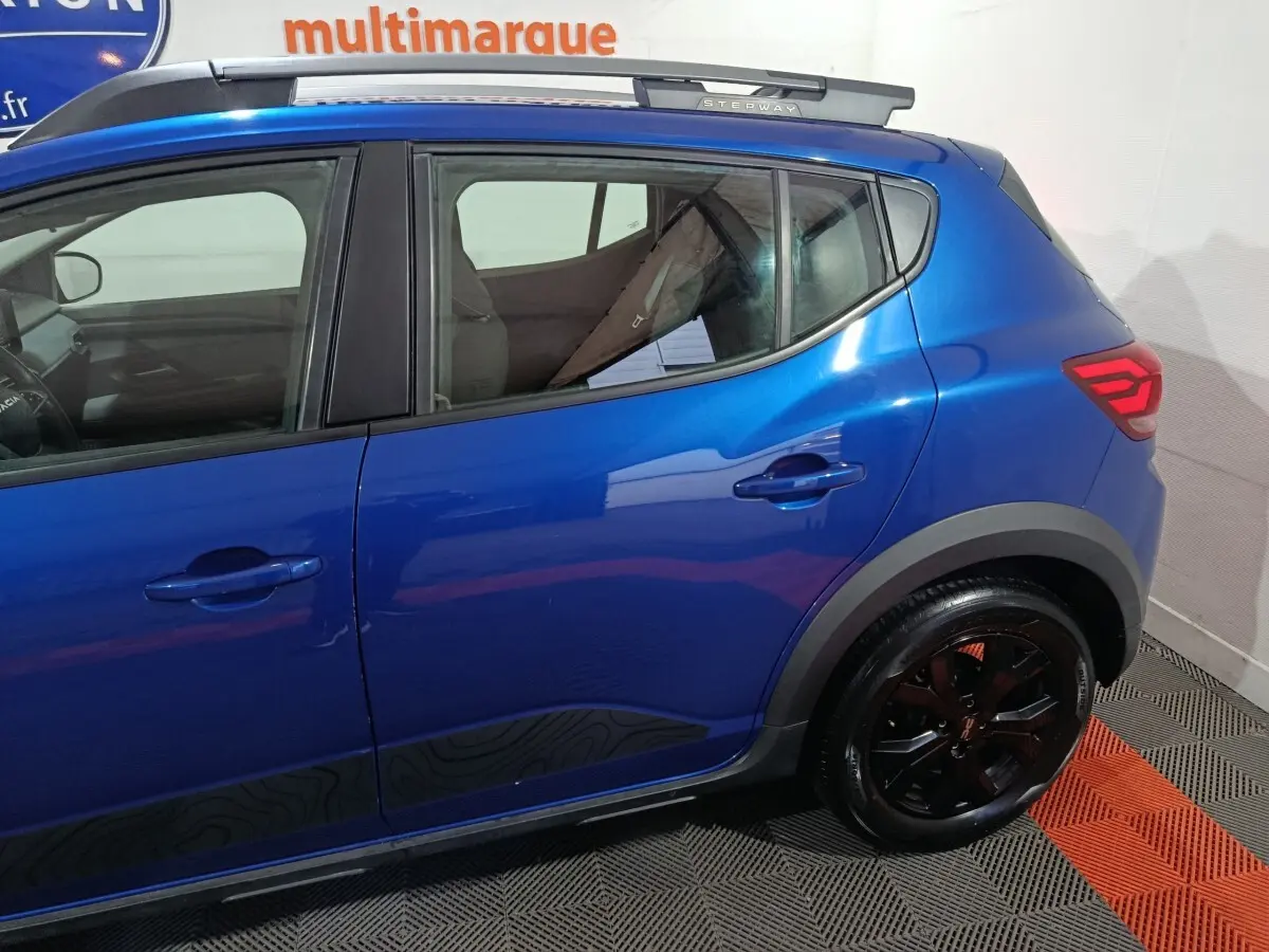 Vue latérale droite d'une Dacia Sandero Extreme+ TCe 110 2024 bleu avec jantes noires et barres de toit assorties.