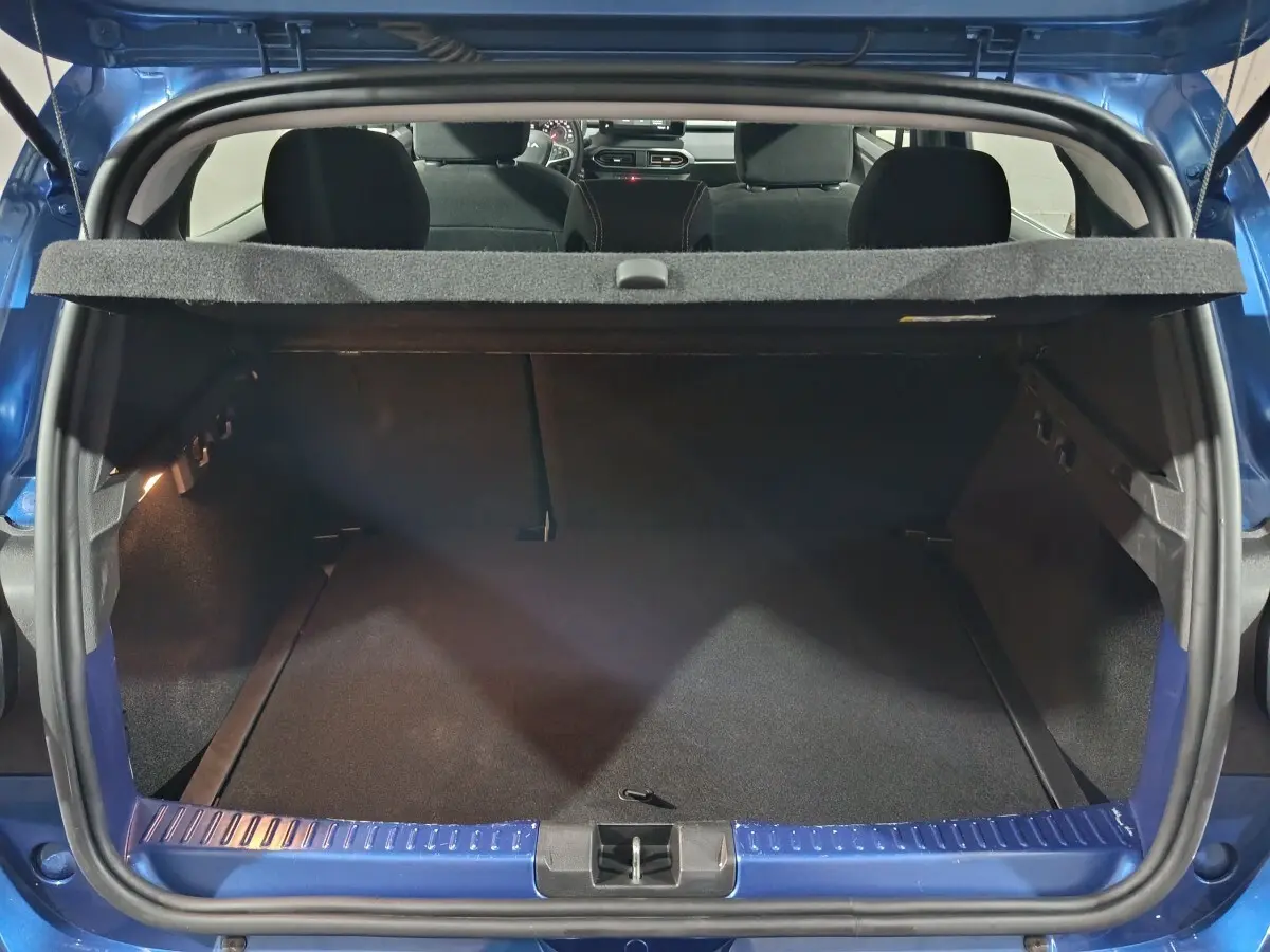 Coffre ouvert vu de l'arrière d'une Dacia Sandero Extreme+ TCe 110 bleu 2024, intérieur noir et tablette de coffre visible.