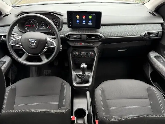 Vue intérieure frontale du tableau de bord de la Dacia Sandero 2023, avec volant, écran tactile et levier de vitesse manuel.
