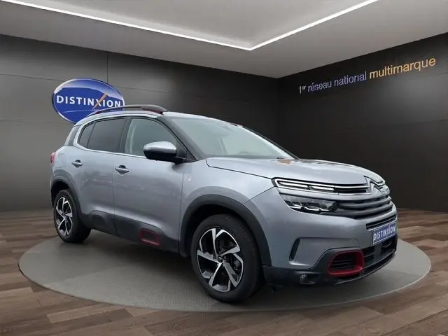 Citroën C5 Aircross gris clair en 3/4 avant droit, avec détails rouges sur boucliers et jantes stylisées.