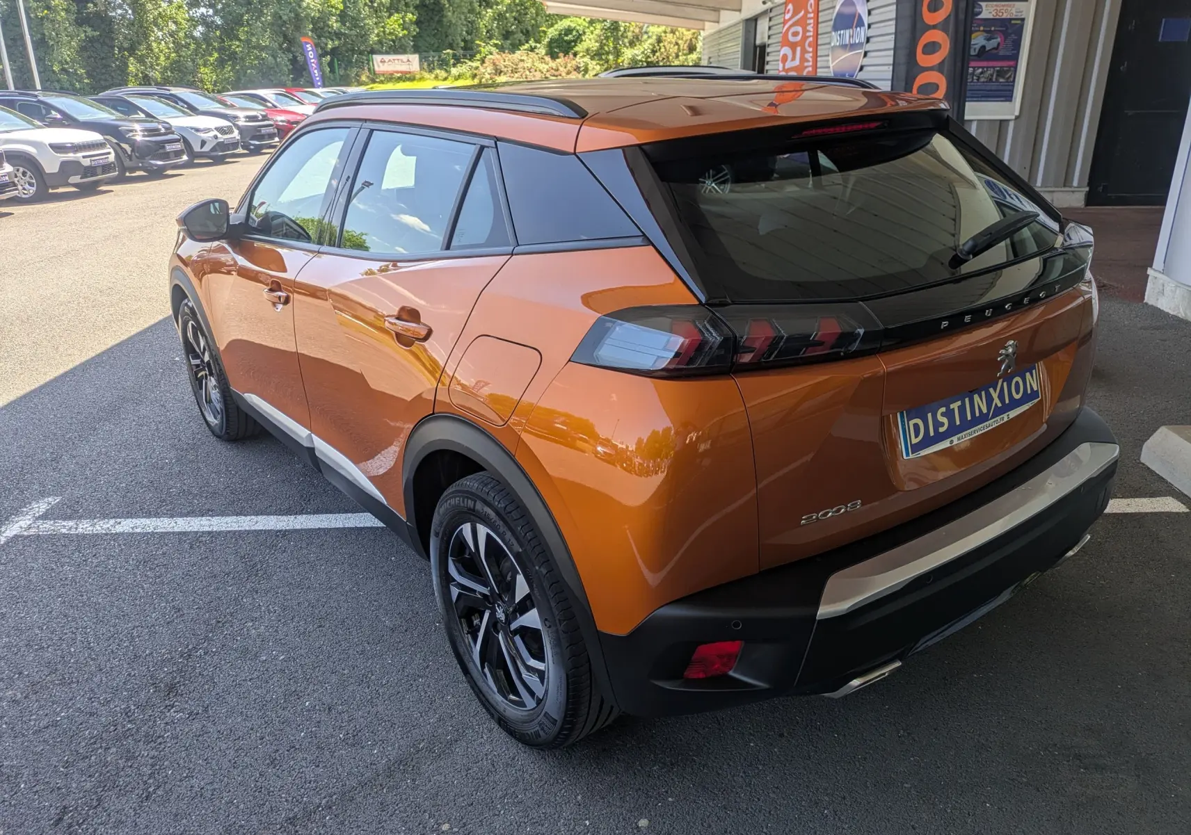 Vue 3/4 arrière droite d'un Peugeot 2008 orange 2021 avec jantes noires bicolores et toit noir, stationné en extérieur.