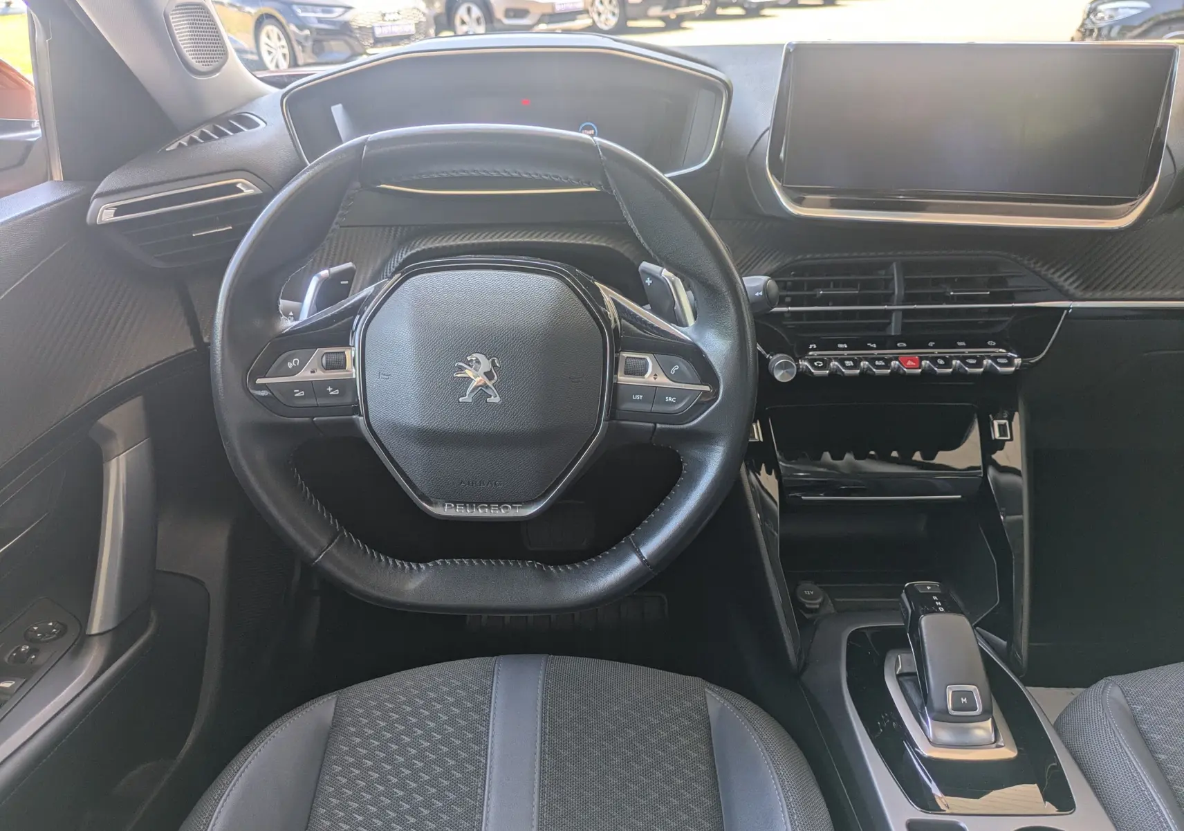 Vue intérieure centrée sur le volant compact et le tableau de bord moderne du Peugeot 2008, avec écran tactile et commandes intégrées.