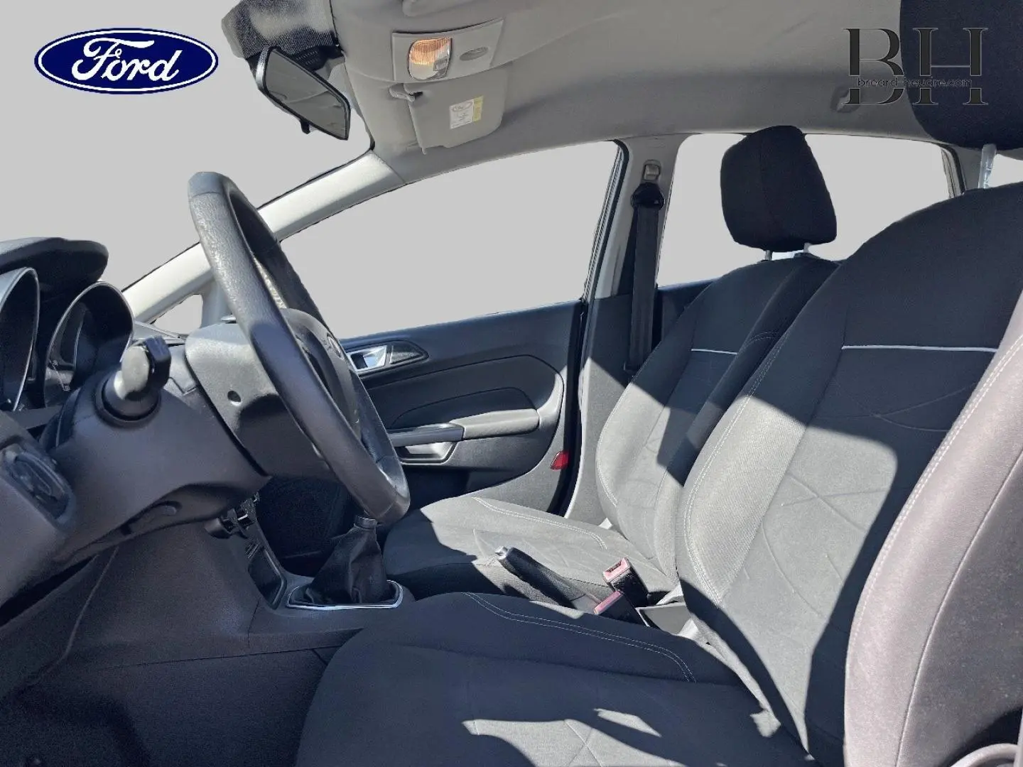 Vue intérieure côté conducteur de la Ford Fiesta 1.5 TDCi 75ch Edition 2015 avec sièges tissu noirs et volant cuir multifonction.