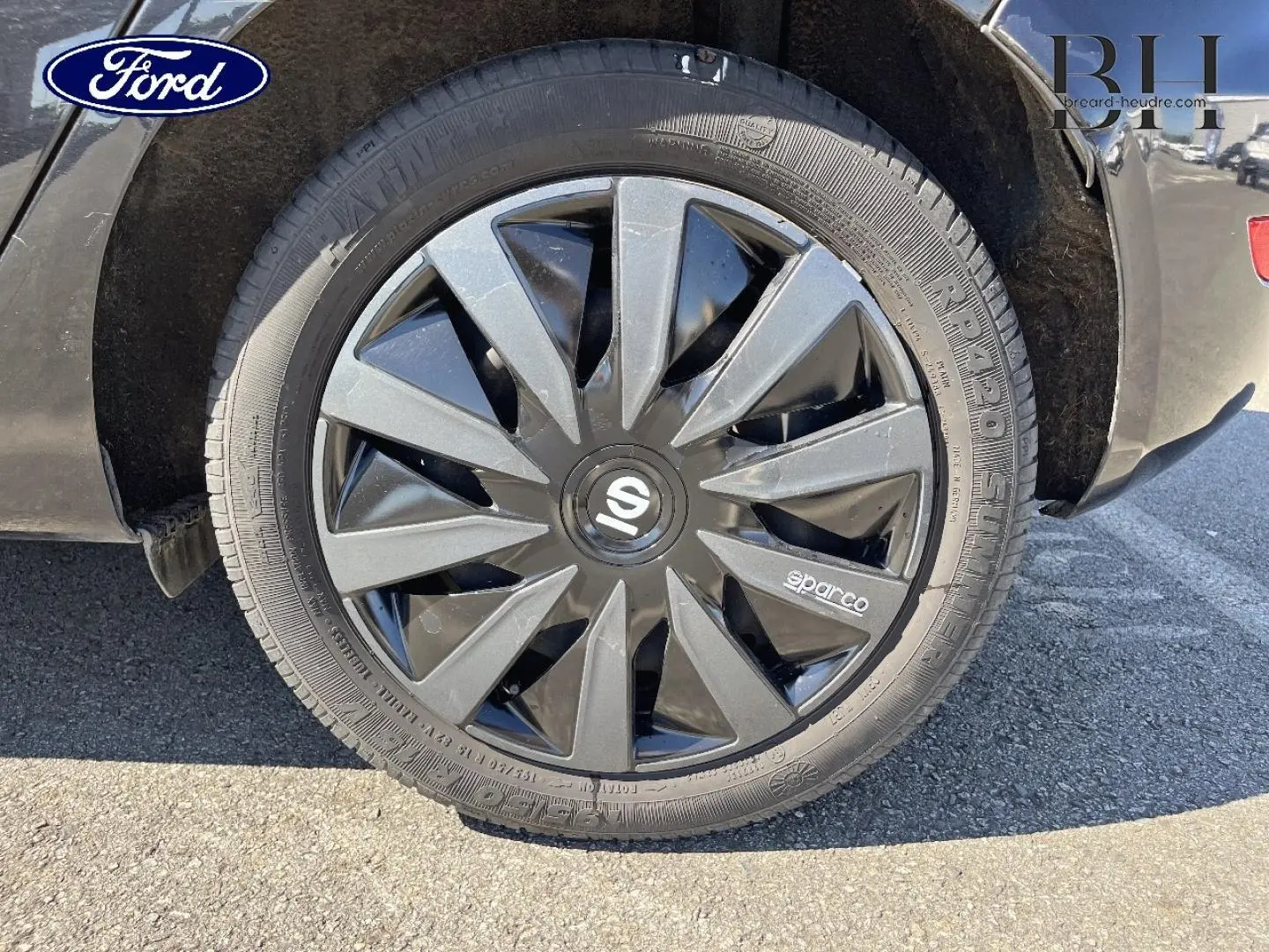 Gros plan sur la roue arrière droite noire Scala d'une Ford Fiesta 2015 avec enjoliveur Sparco gris et noir.