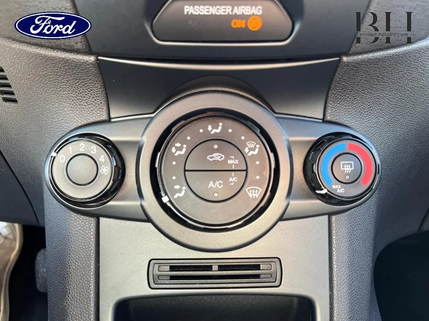 Gros plan sur les commandes de climatisation manuelle d’une Ford Fiesta noire, avec réglages ventilation et température visibles.