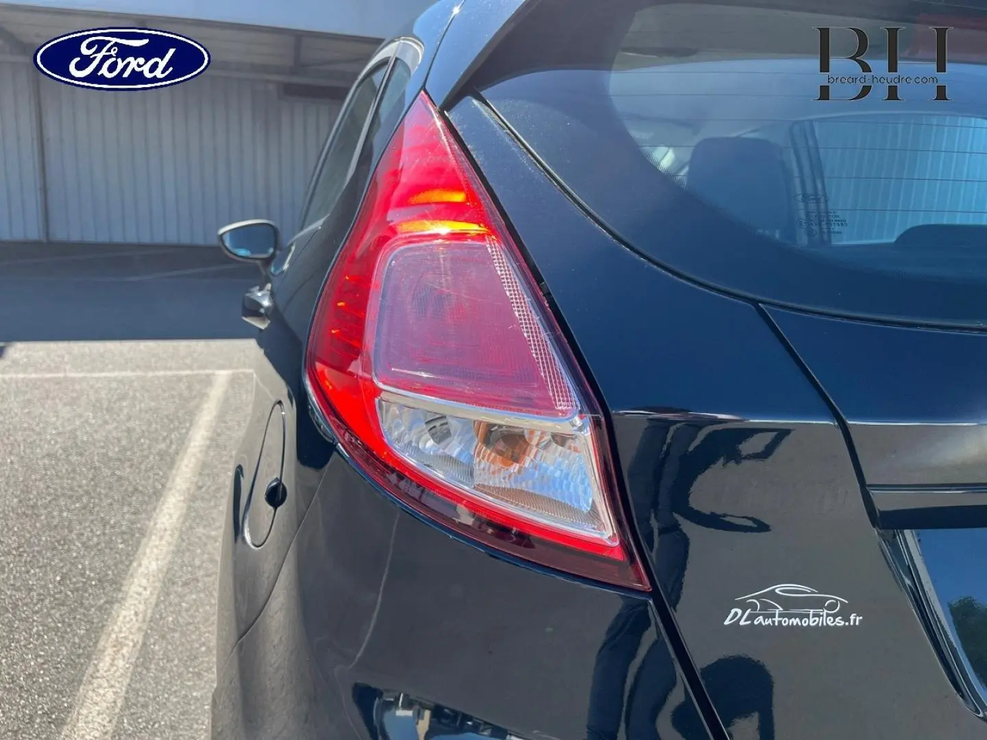 Vue 3/4 arrière gauche d'une Ford Fiesta noire Scala avec feu arrière distinctif et logo DLautomobiles.fr sur le coffre.
