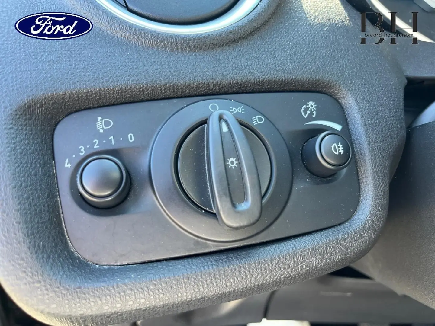Gros plan sur le bouton de commande des phares du tableau de bord d'une Ford Fiesta noire, avec réglage d'intensité et feux antibrouillard.