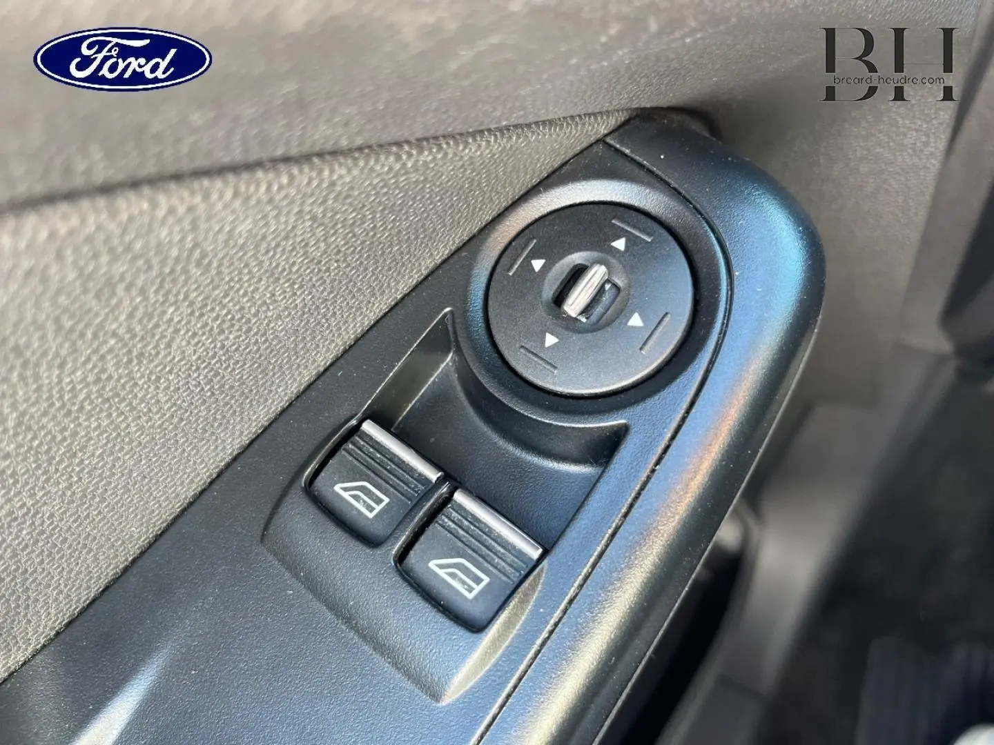 Gros plan sur les commandes électriques des vitres et réglage des rétroviseurs côté conducteur d'une Ford Fiesta noir Scala.