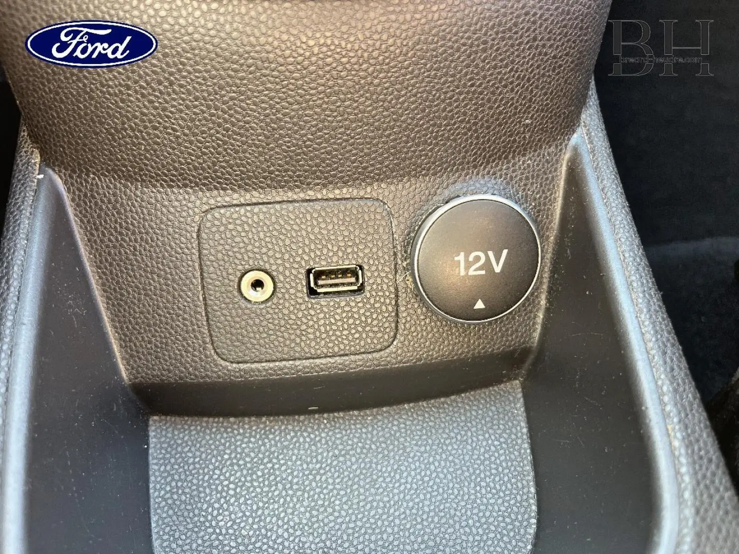 Vue rapprochée de la prise 12V, port USB et entrée auxiliaire sur la console centrale d'une Ford Fiesta noire.