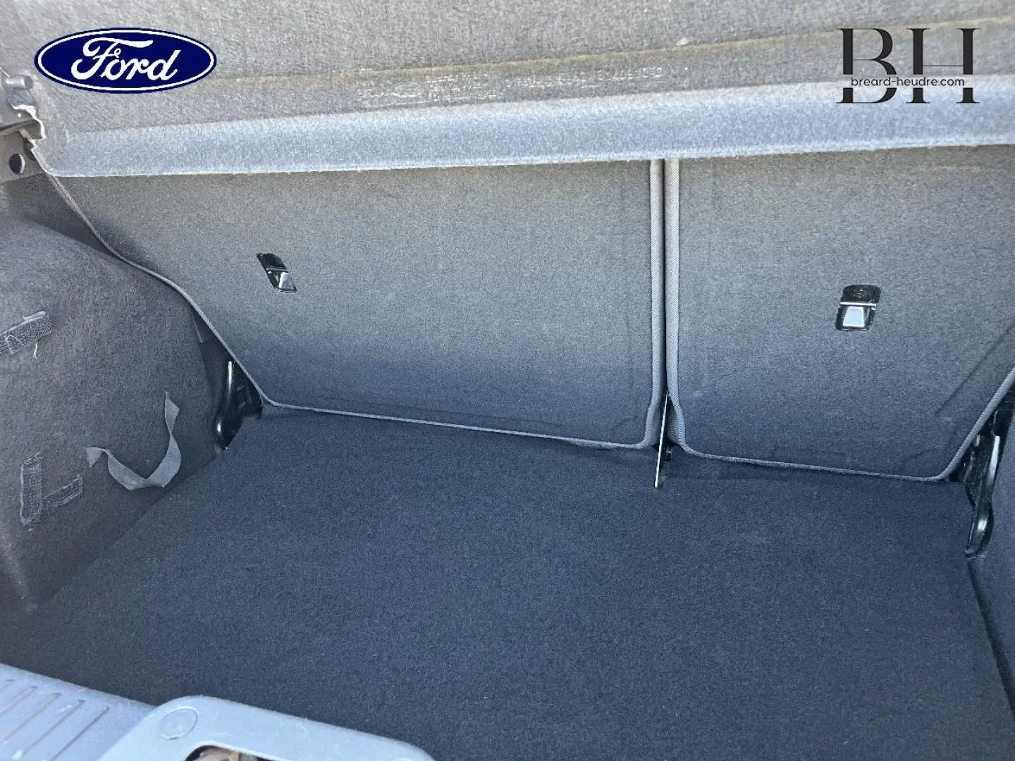 Coffre ouvert de la Ford Fiesta noir Scala, vue intérieure montrant la banquette arrière rabattable et le tapis de coffre.