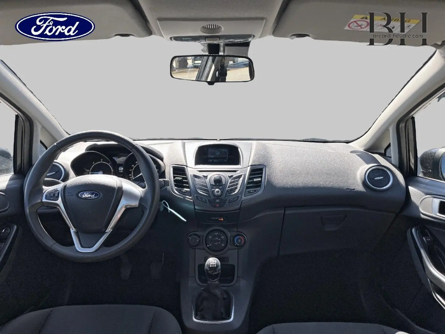 Vue frontale de l'intérieur noir de la Ford Fiesta 2015, montrant le volant multifonction et la console centrale avec écran.