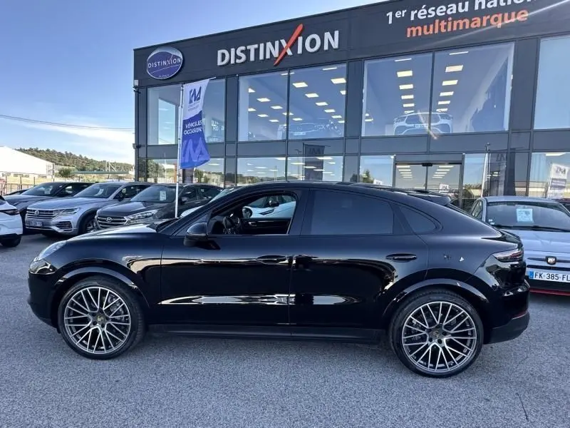 Vue de profil côté gauche d'un Porsche Cayenne Coupé noir métal 2020 avec jantes alliage distinctives, stationné devant un concessionnaire.