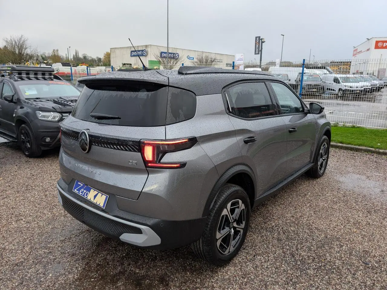Vue 3/4 arrière droite d'un Citroën C3 Aircross gris métallisé avec toit noir et feux arrière LED allumés.