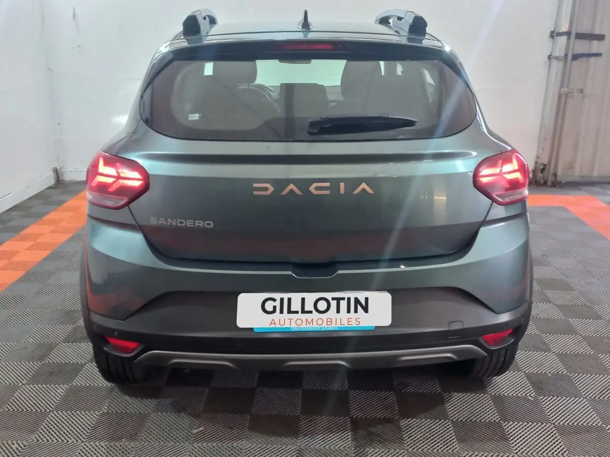 Vue arrière d'une Dacia Sandero Extreme+ TCe 110 2024 vert foncé avec feux LED allumés en intérieur.