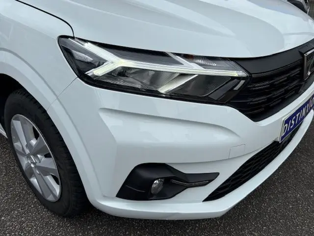 Gros plan sur l'avant droit blanc glacier du Dacia Sandero 2023, mettant en valeur le phare LED et la calandre noire.