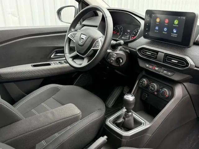 Vue intérieure côté conducteur de la Dacia Sandero 2023, tableau de bord moderne avec écran tactile et boîte manuelle.