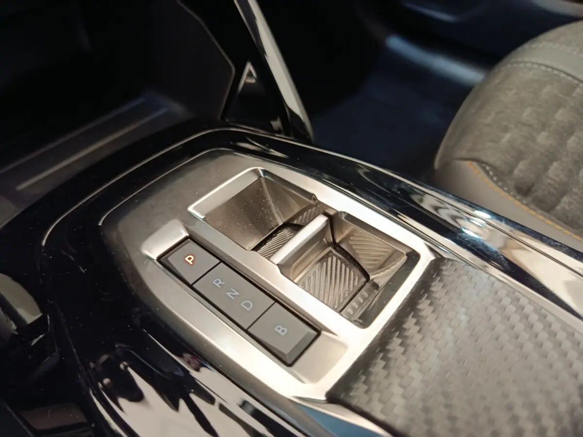 Gros plan sur la console centrale noire brillante avec levier de vitesses automatique de la Peugeot 208 électrique gris clair.