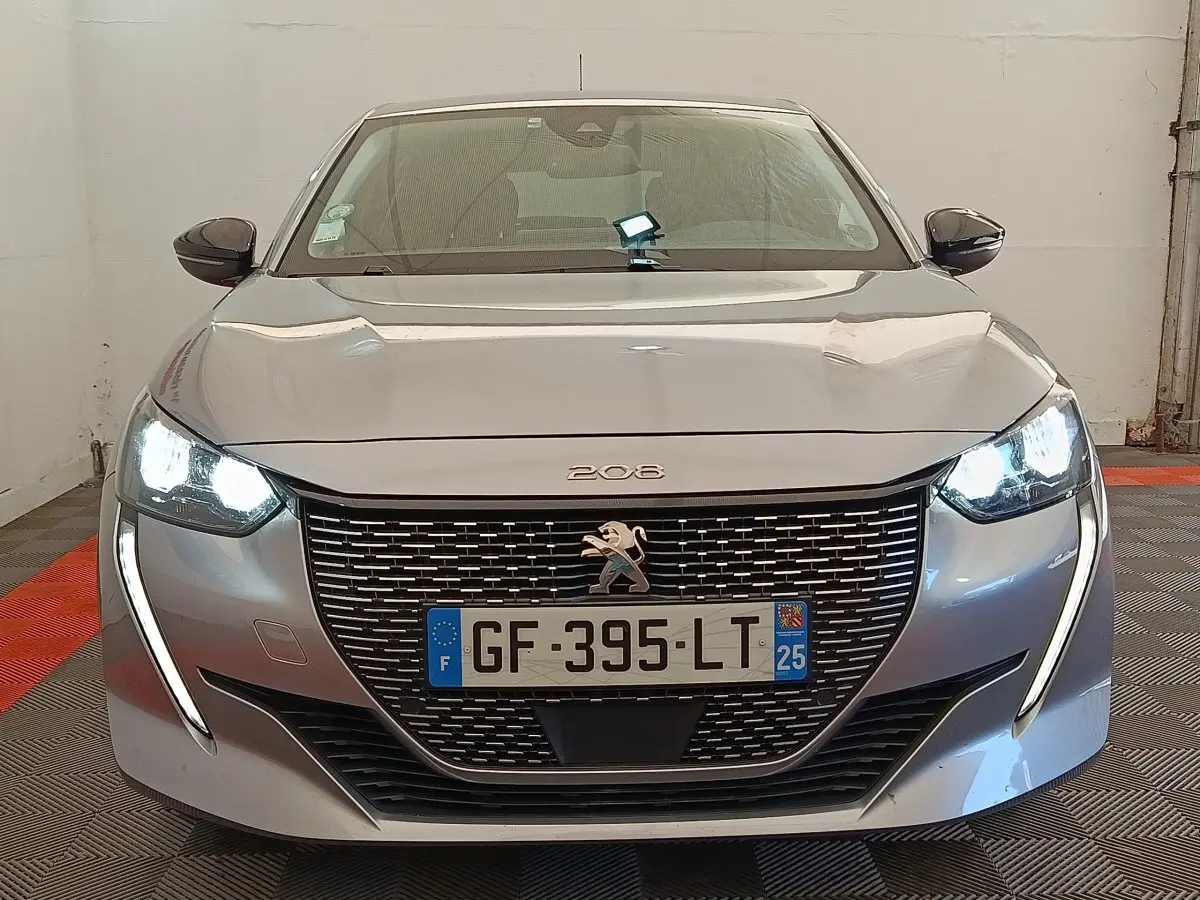 Vue de face du Peugeot 208 Electrique Roadtrip gris clair avec phares LED allumés et calandre distinctive.