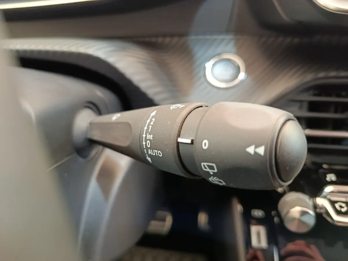 Gros plan sur la commande d’essuie-glace à gauche du volant dans l’habitacle d’une Peugeot 208 électrique gris clair.
