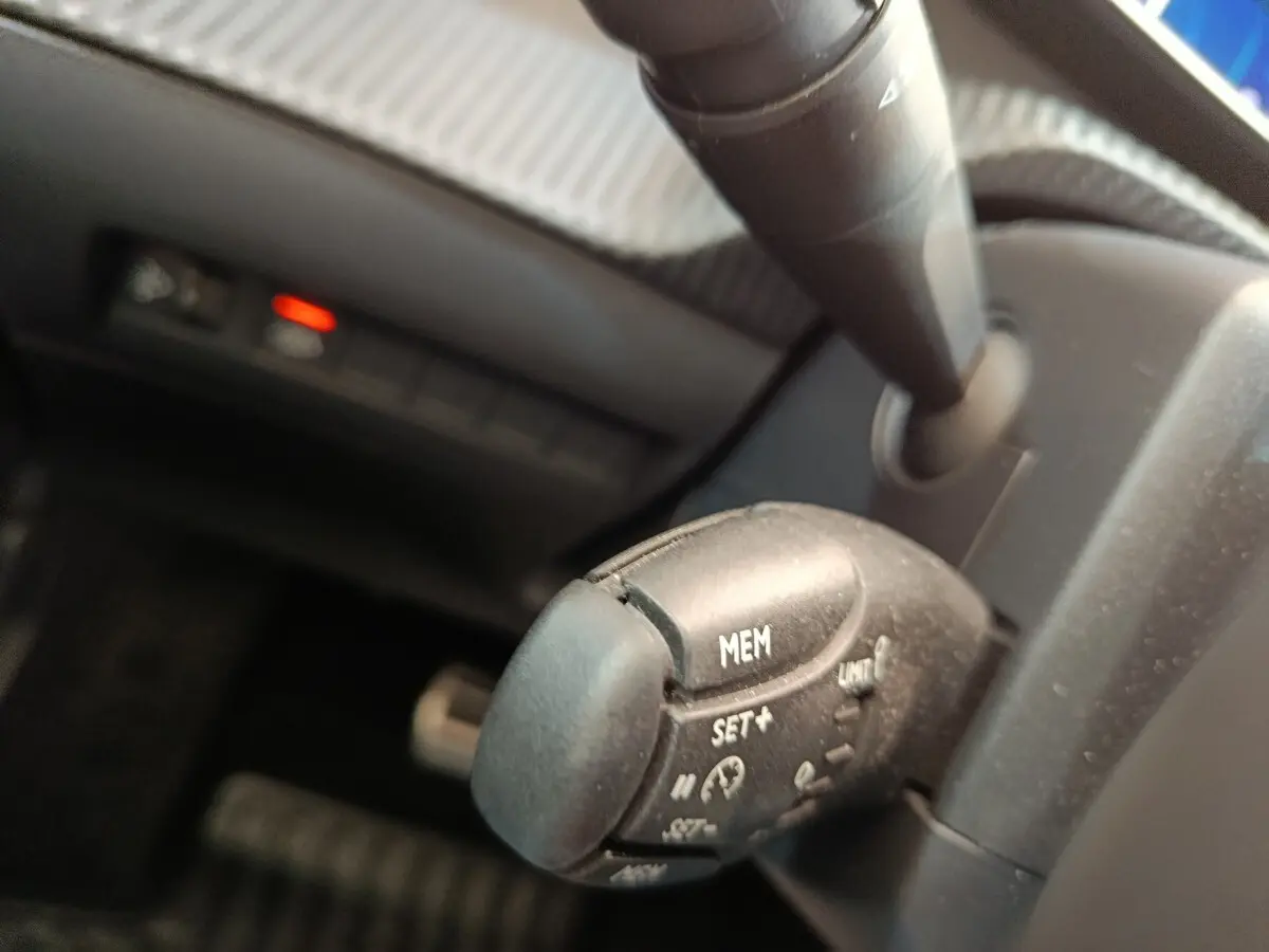 Gros plan sur la commande de régulateur de vitesse noire dans l’habitacle d’une Peugeot 208 électrique gris clair.