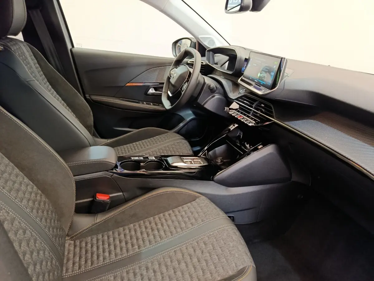 Intérieur avant droit de la Peugeot 208 électrique, sièges gris, tableau de bord avec écran tactile et volant cuir.