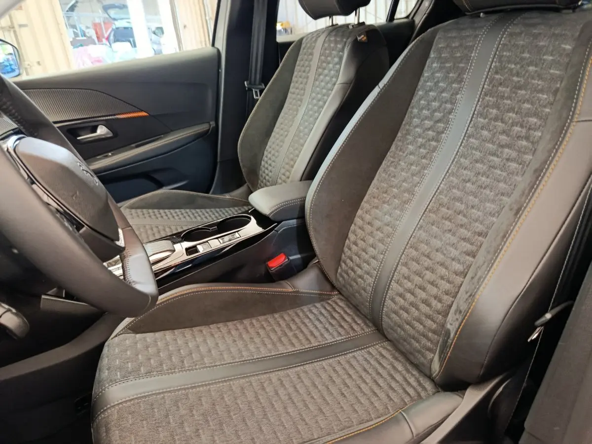 Vue intérieure côté conducteur des sièges avant gris foncé avec surpiqûres orange et volant cuir de la Peugeot 208 Electrique Roadtrip 2022.