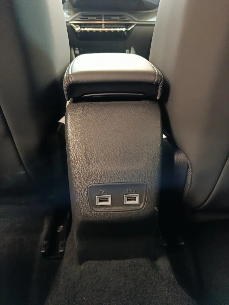 Vue rapprochée de la console centrale arrière noire avec deux ports USB dans l’habitacle d’une Peugeot 208 électrique gris clair.
